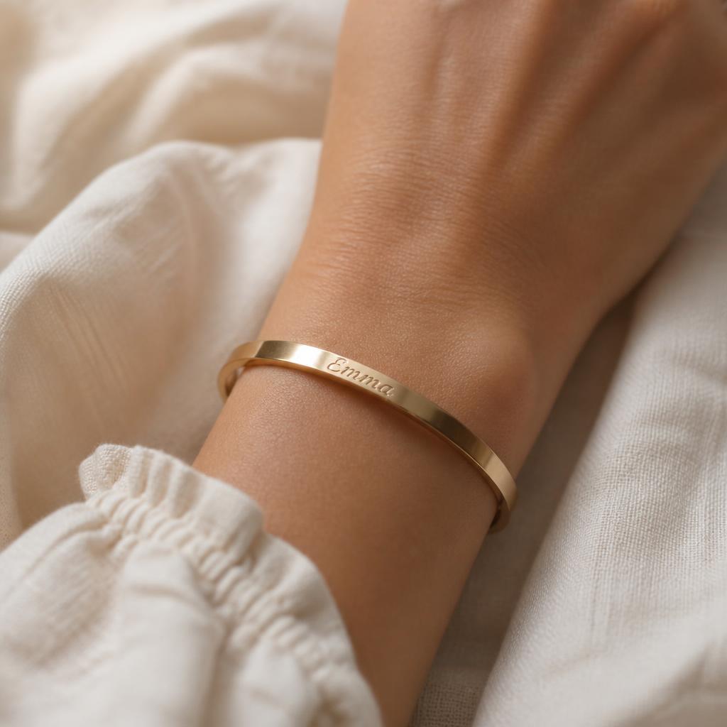 Woman's wrist wearing a gold bangle engraved with the name Emma